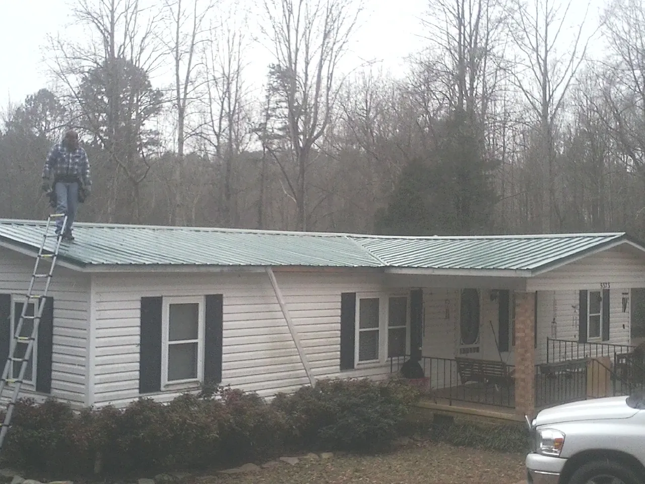 Worker on a ladder beside a new green metal roof on a ranch home in Selma