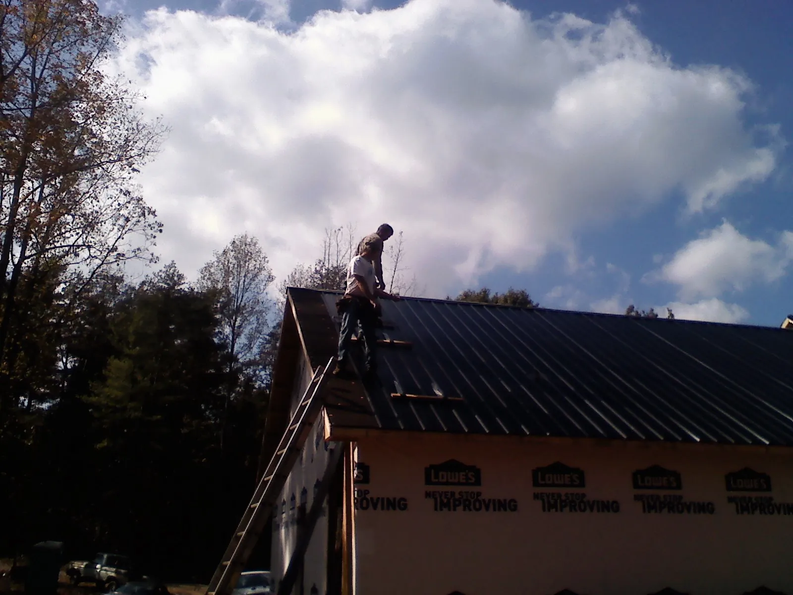 Roofer fastening dark metal panels high against a cloudy sky, from a Roof Inspection job in Selma